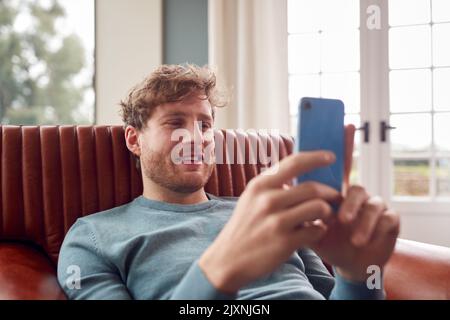 Man Sitting Relaxing On Armchair At Home Using Mobile Phone Stock Photo