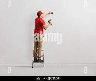 Worker standing on a ladder and installing a security camera on a wall Stock Photo