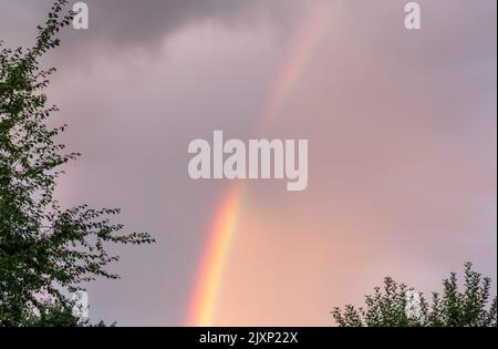 Close up view of rainbow in cloudy evening summer sky. Stock Photo