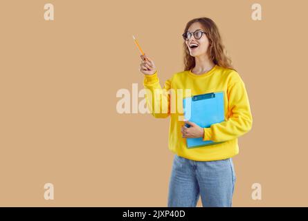 Funny, happy student or teacher standing on beige background and pointing pencil at copy space Stock Photo