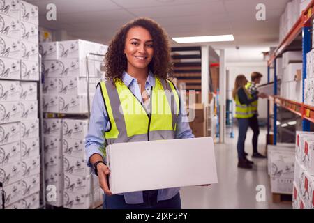 Portrait Of Female Worker Inside Busy Warehouse Carrying Box Stock Photo