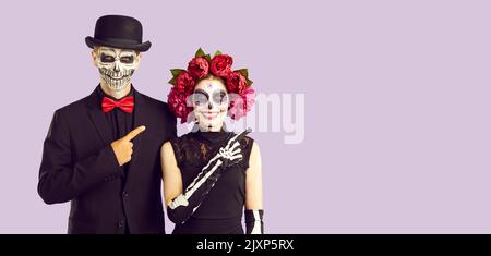 Couple in creative costumes pointing finger at copy space recommending something Halloween themed. Stock Photo