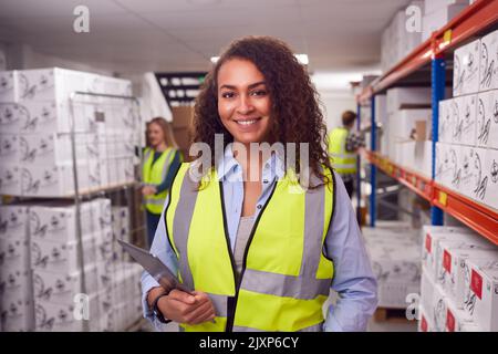 Portrait Of Female Worker Inside Busy Warehouse Checking Stock On Shelves Using Digital Tablet Stock Photo