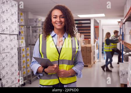 Portrait Of Female Worker Inside Busy Warehouse Checking Stock On Shelves Using Digital Tablet Stock Photo