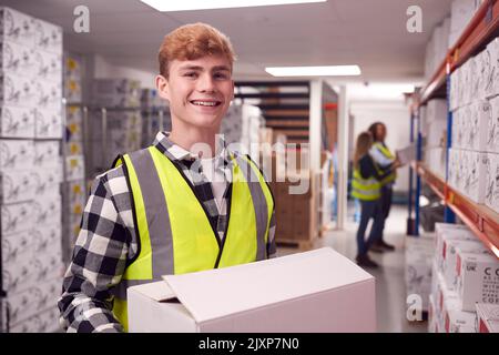 Portrait Of Male Worker Inside Busy Warehouse Carrying Box Stock Photo