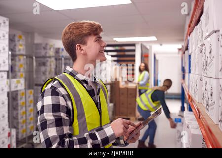 Male Worker Inside Busy Warehouse Checking Stock On Shelves Using Digital Tablet Stock Photo