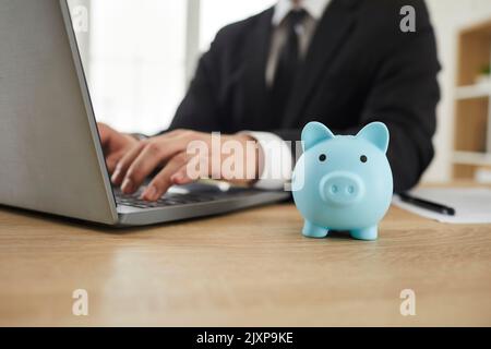 Piggy bank on the office desk of a businessman working on his laptop in the background Stock Photo