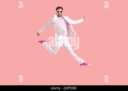 Full length shot of funny young man in suit jumping high in the air isolated on pink background Stock Photo