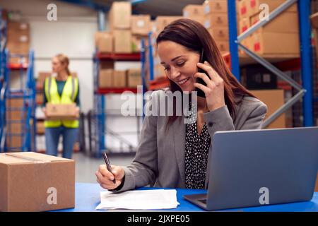 Female Team Leader Working On Laptop Talking On Mobile Phone Stock Photo