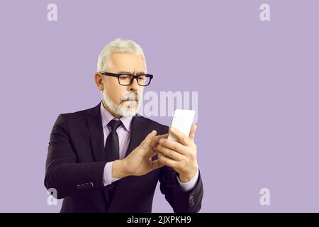 Studio portrait of serious senior businessman in suit and glasses using mobile phone Stock Photo