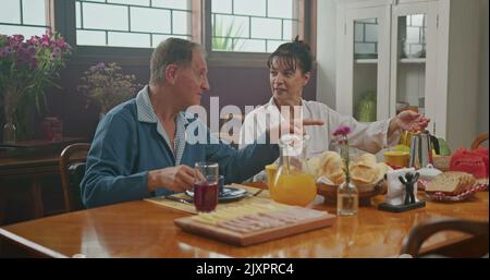 Married couple having breakfast together. The wife serves coffee to her husband. the two chat happily and enjoy a good cup of coffee wearing pajamas Stock Photo