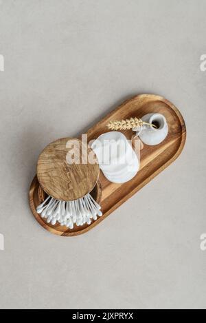 Сotton buds in wooden box with round facial cotton pads on wooden tray on a light concrete background, top view Stock Photo