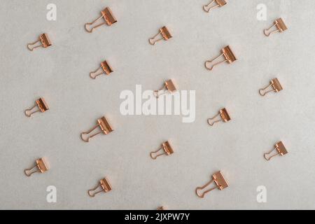 Golden paper binder clips pattern on light concrete background, top view. Office supplies background Stock Photo