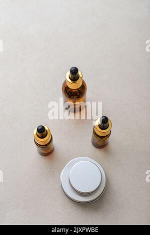 Dropper brown glass bottles, metal round tin cosmetic cans and small plastic can on light concrete background, top view Stock Photo