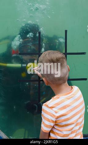 Young Boy Playing Noughts And Crosses, Tic Tac Toe Game Against A Royal Navy Diver Wearing Scuba Equipment In A Tank Of Water, Bournemouth UK Stock Photo