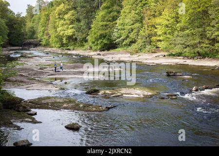 Children play on the exposed rocks of the fast flowing River Ericht, Blairgowrie, Scotland. Stock Photo