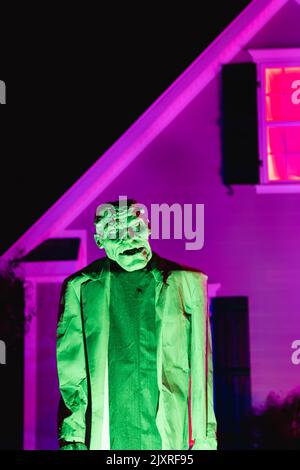 A scary life sized Frankenstein snimated monster glowing green against a purple lit house in October on Haloween Stock Photo