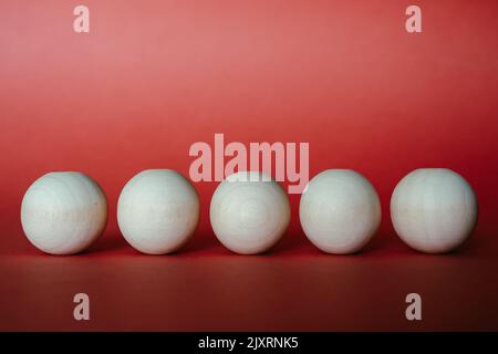 View of five equidistant separated wooden balls on red background. Graphic resource Stock Photo