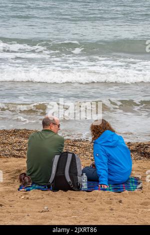 couple sitting on the beach together, older couple chatting while sitting on the beach, couple at the seaside, waves crashing onto beach at swanage. Stock Photo