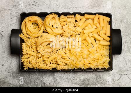 Assorted dry noodles in a rectangular black serving platter with handles on a stone background in a top view Stock Photo