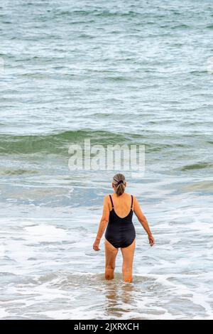 older lady wild swimming in the sea, older lady having a dip in the sea, lady wearing black swimming costume wild swimming, female wild swimmer in sea Stock Photo