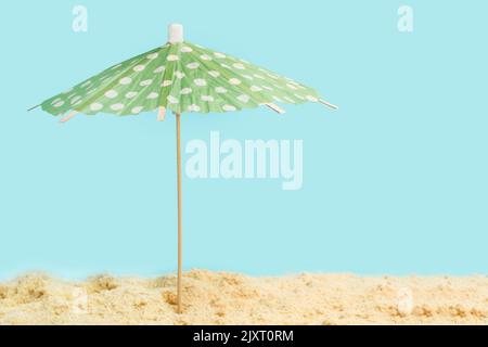 A green with white polka dots umbrella on the sand and on a light blue background Stock Photo
