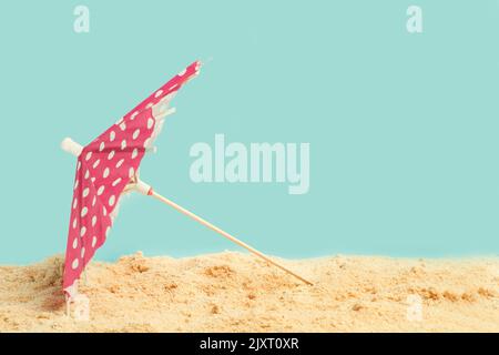 A red with white polka dots open umbrella on the sand and on a light blue background Stock Photo