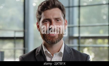 Adult calm strong confident Caucasian 40s bearded man looking at camera with serious expression smiling dental toothy company CEO leader manager Stock Photo