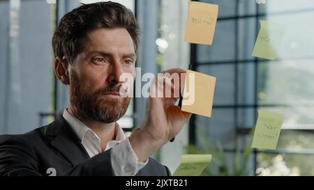 Close up busy focused smart male manager worker CEO boss planning work strategy pensive thoughtful bearded Caucasian businessman writing ideas on Stock Photo