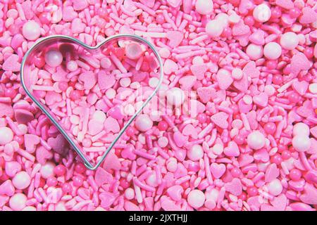 Full frame pink heart sprinkles and a metal heart shape, copy space Stock Photo