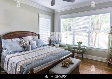 A spacious bedroom with a dark wood bed and dresser or chest and a fan and chaisse chair Stock Photo