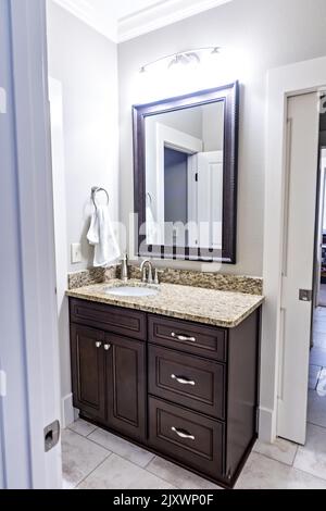 A modern new construction small guest bathroom with espresso cabinets, granite countertops, a tile floor and a mirror Stock Photo