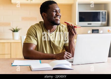 african american man in beige t-shirt record voice message by mobile cell phone at home Stock Photo