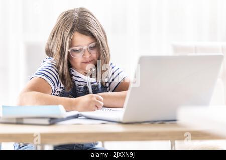 Girl in glasses writes down notes studing via distant learning over the internet. Stock Photo
