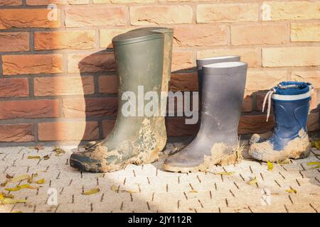 Three dirty boots of all family members. Working shoes placed on the concrete pavement. Boots of child and parents. Children help with gardening. Stock Photo