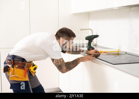 craftsman installs hob in kitchen. Household Appliance Installation Services Concept Stock Photo