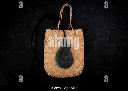 Pounamu fish hook necklace on weaved bag on dark background. Aotearoa, New Zealand, Maori. Stock Photo