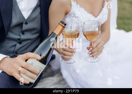Close up cropped unrecognizable groom and bride hands drinking and pouring bubbly champagne wine from bottle and glasses Stock Photo
