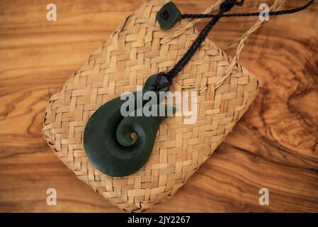 Pounamu fish hook necklace on grainy wooden background. Aotearoa, New Zealand, Maori. Side angle view. Stock Photo