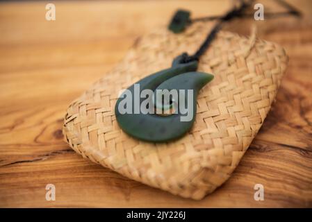 Pounamu fish hook necklace on grainy wooden background. Aotearoa, New Zealand, Maori. Side angle view. Stock Photo