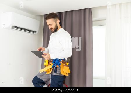 male technician service worker diagnosing for repairs air conditioner. person using tablet. Stock Photo