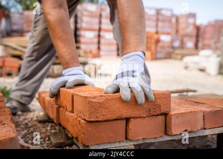 Close up on hands of unknown caucasian man construction industry or warehouse worker stacking clay brick on the palette Stock Photo
