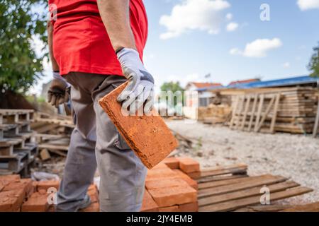 midsection of unknown caucasian man male construction or warehouse worker carry or hold clay bricks while stand outdoor in sunny day copy space Stock Photo