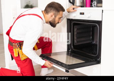 repairman examining oven with screwdriver in kitchen with tool case Stock Photo