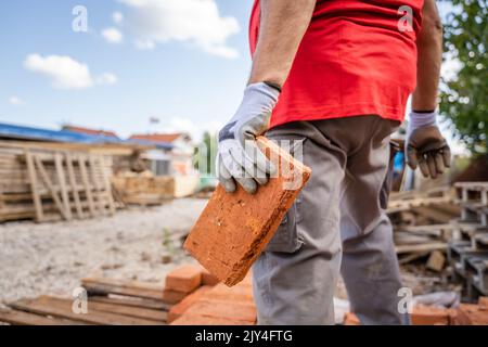 midsection of unknown caucasian man male construction or warehouse worker carry or hold clay bricks while stand outdoor in sunny day copy space Stock Photo