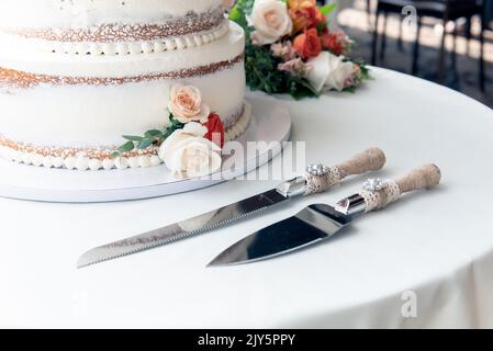 Wedding cake is set next to stainless steel utensil serving set for bride and groom to cut a slice of cake. Stock Photo