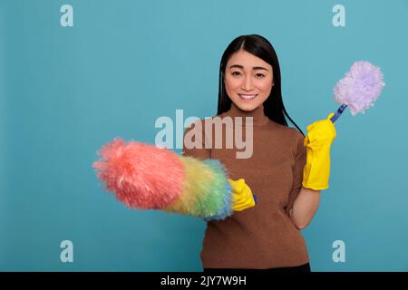 Laughing glad and smiling asian young housekeeper from chores holding two duster brush in yellow gloves, Cleaning home concept, Woman feeling positive from day to day work Stock Photo