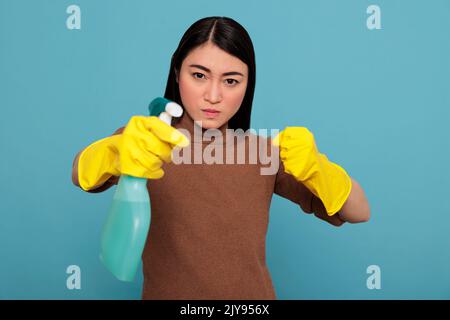 Aggressive overwhelmed asian young housemaid in rubber gloves and detergent spray standing in a fight pose, Cleaning home concept, Confidence energetic housekeeper feeling negative Stock Photo