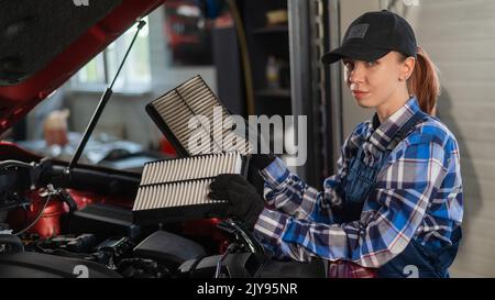 Caucasian female auto mechanic changes the engine air filter in the car. Stock Photo