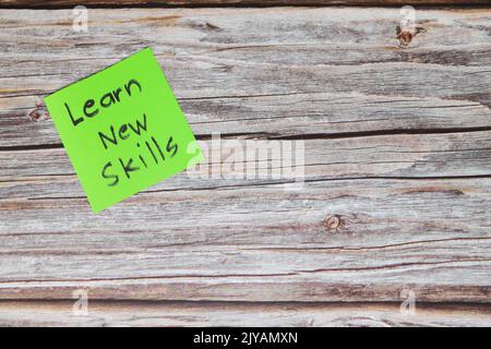Learn new skills for self improvement and personal development concept. Green sticky note reminder in wooden background with copy space. Stock Photo